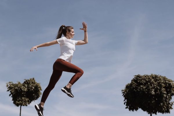 Athletic woman in action jump against a blue sky background. Captures fitness in motion.